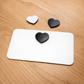Two black heart-shaped objects and one white heart-shaped object on a white card against a wooden background.